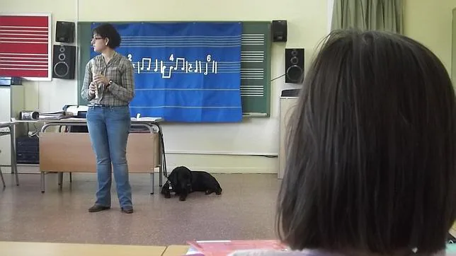 La imagen muestra a la maestra con una flauta en la mano y el perro guía junto a ella