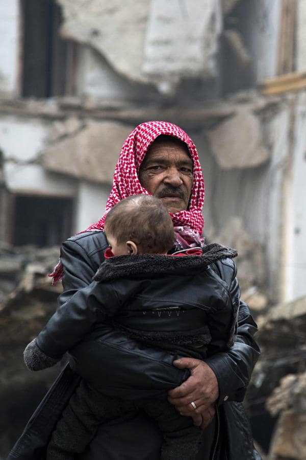 Un hombre deja un barrio del este de Alepo con un niño en brazos